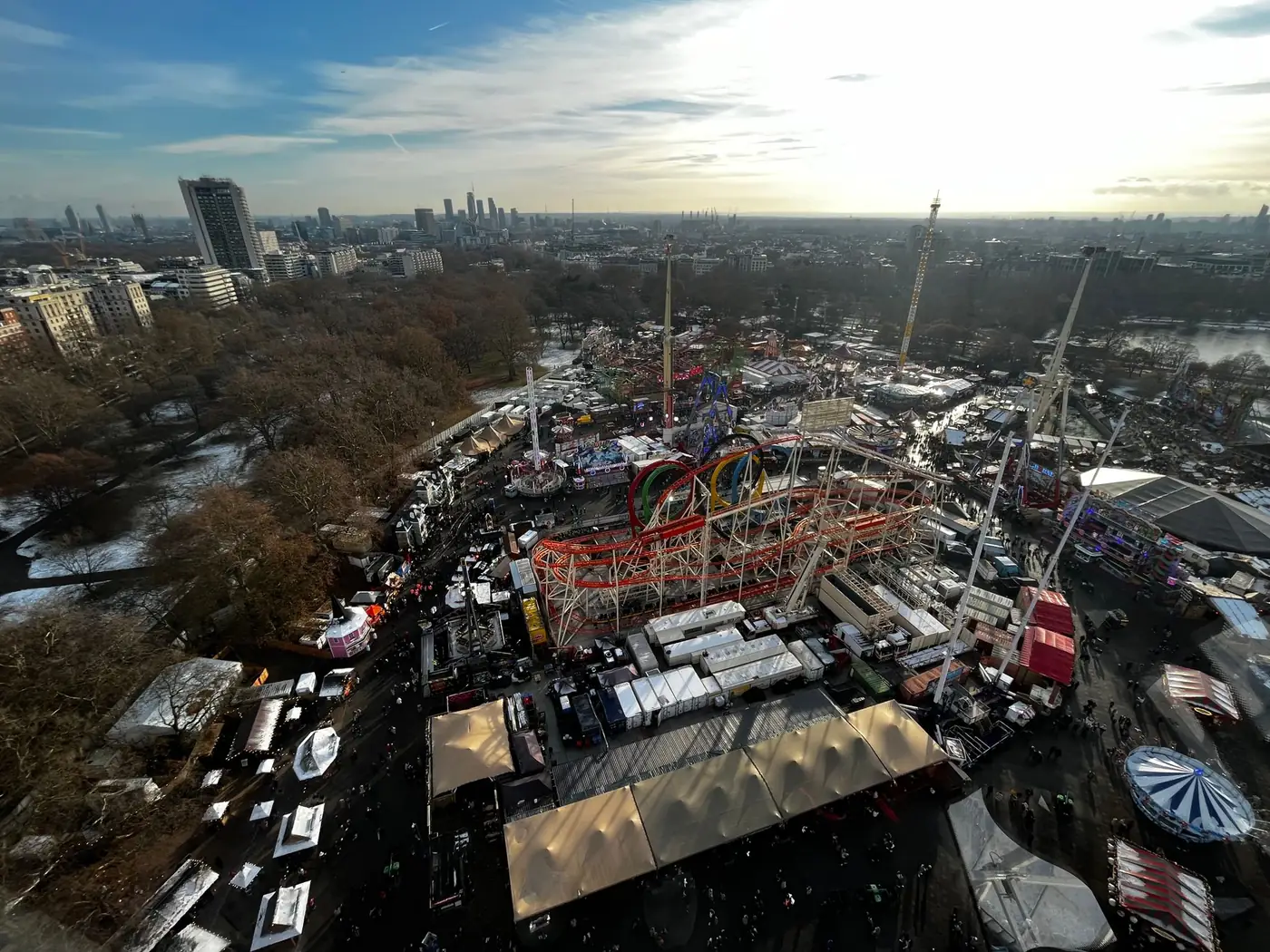 Luchtfoto van een verlicht kermis- en marktterrein in een park, met de skyline van Londen op de achtergrond