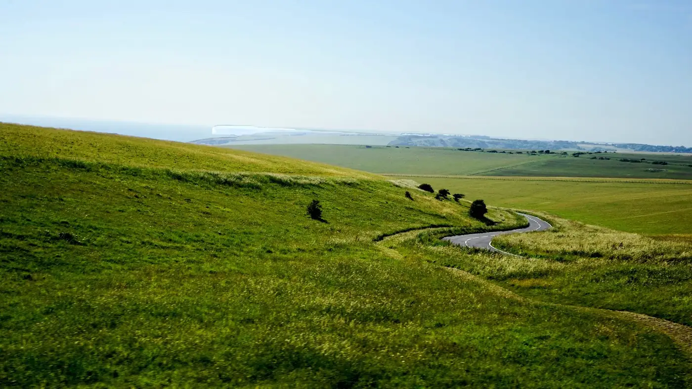 Idyllic countryside view with green fields and a winding road under blue skies.