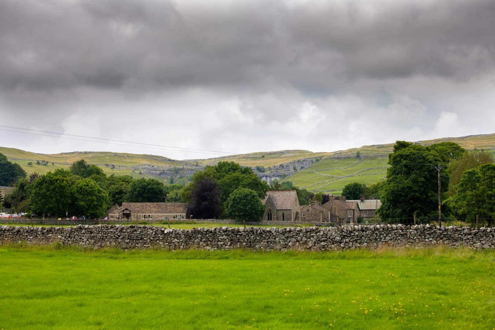 Scenic English rural landscape with stone walls and rolling hills under dramatic skies.
