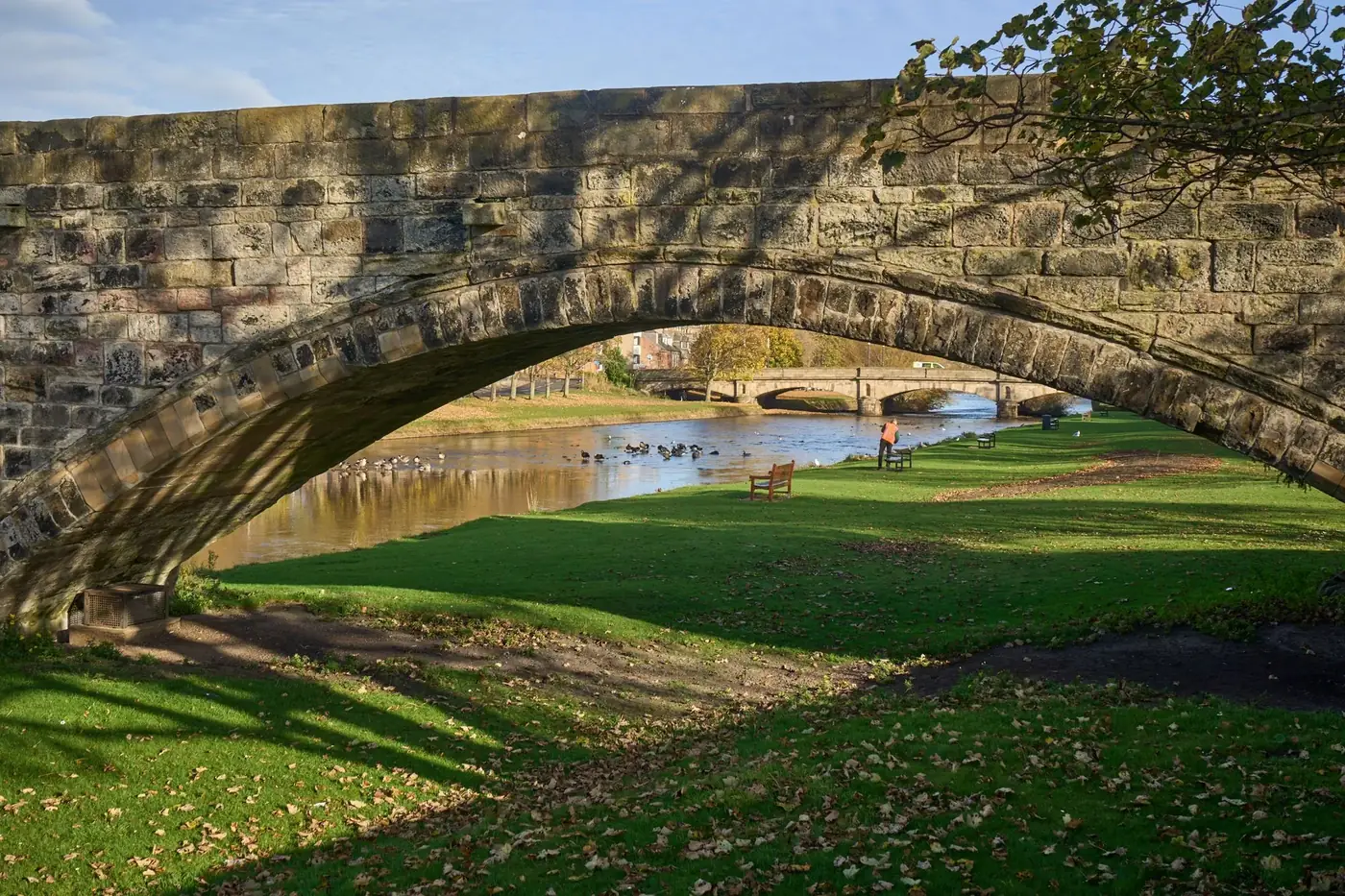 Scenic view of a historic stone bridge in a tranquil park in Scotland during autumn.