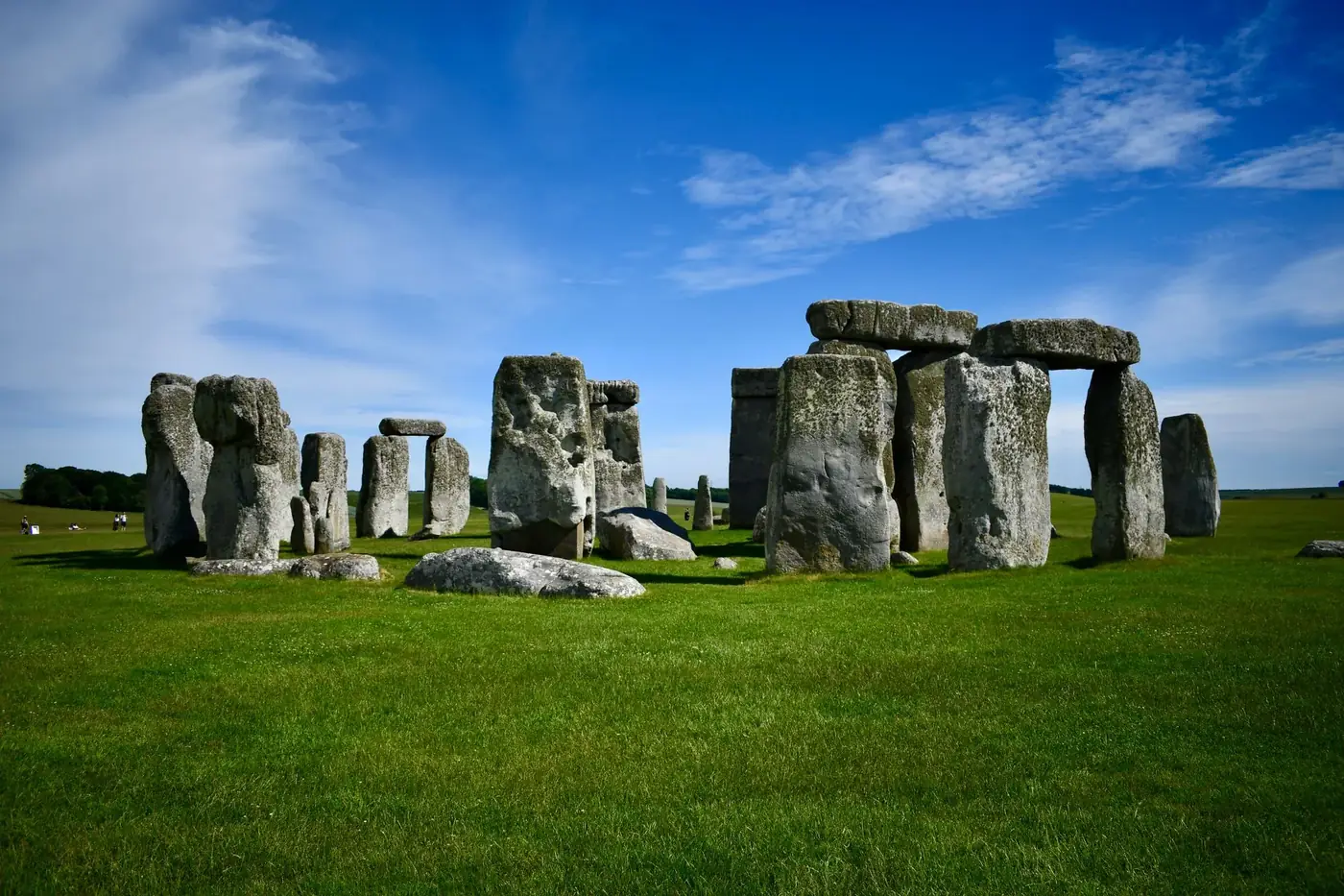 Iconic Stonehenge stones stand tall under a bright blue sky with lush green fields.