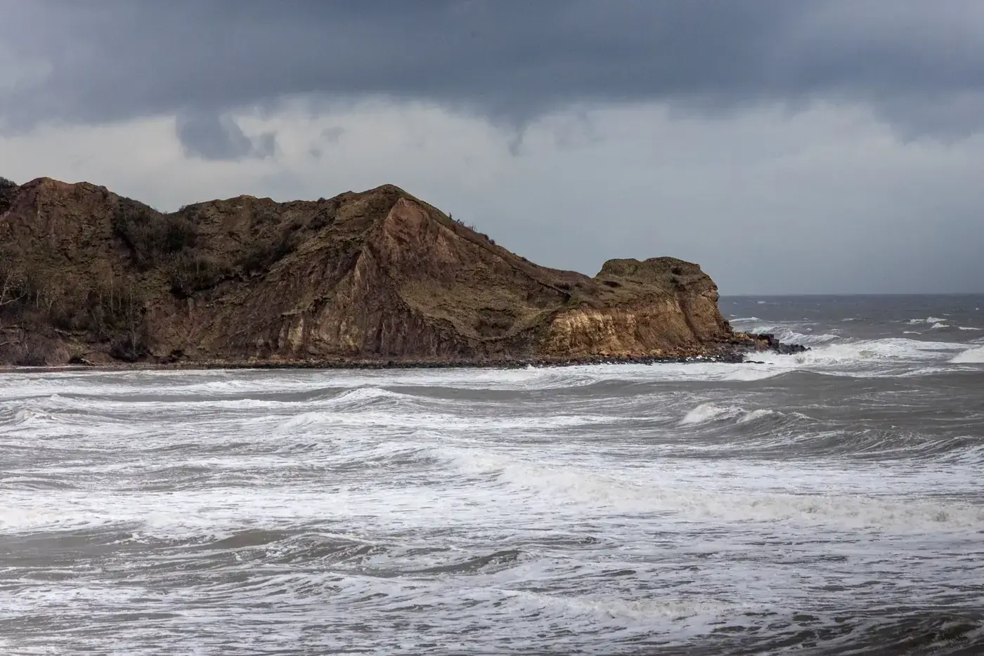 Stormy winter seas crash against the rugged cliffs of Scarborough, UK.